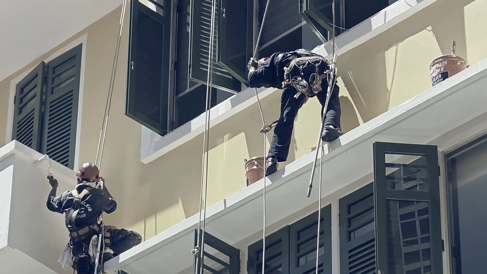 Deux cordistes au travail sur une façade, cordes et seau de chantier